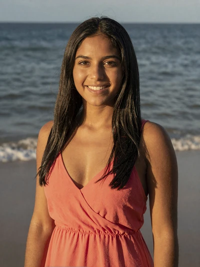 Gabriela, 26-year-old Puerto Rican woman with honey skin and black hair, smiling on San Juan beach in coral sundress